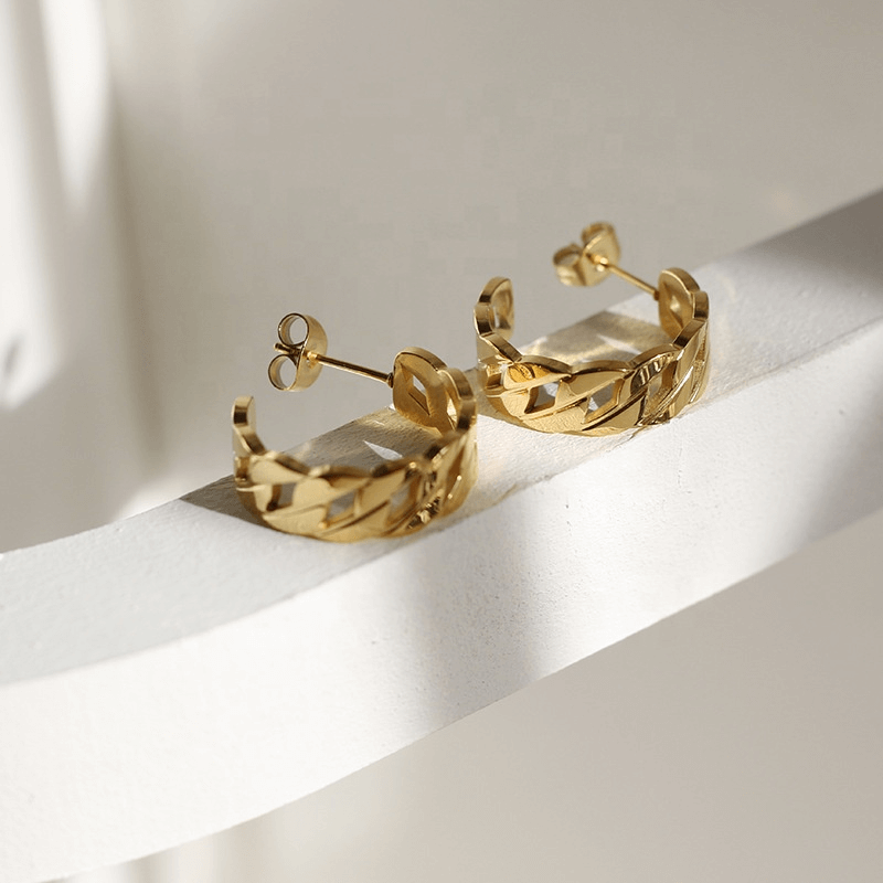 Side view of hollow chain, gold earrings sitting on a white shelf